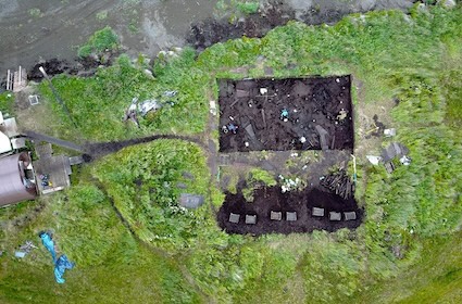 Strong colour contrasted aerial view of an archaeological excavation. Green grass and dark cultural soil.