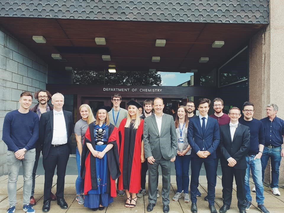 Photograph of a group of people, some in graduation gowns and smart suits.