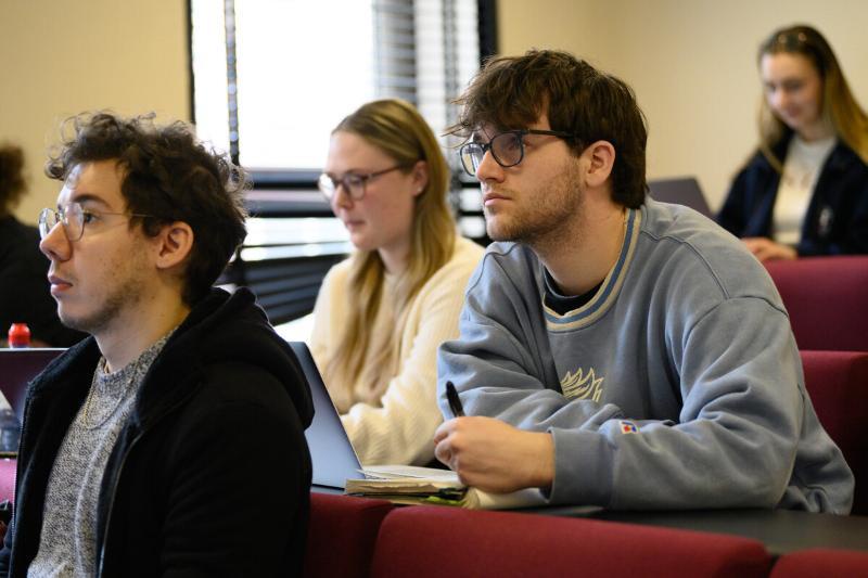 students attend a lecture.  two male students with glasses are in focus