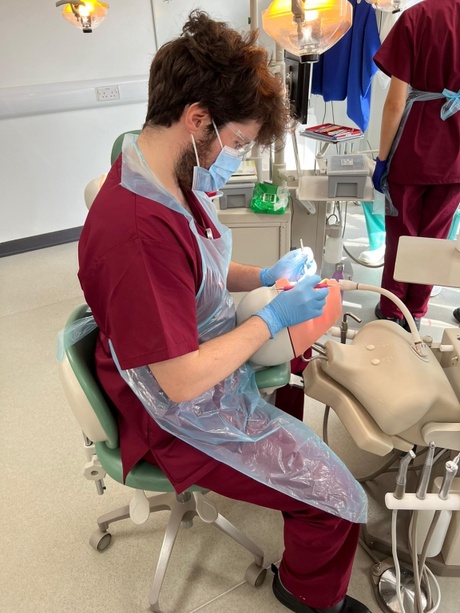 Jay sitting in clinical skills room and doing a procedure on a manekin.