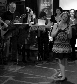 Woman singing in middle of circle of musicians