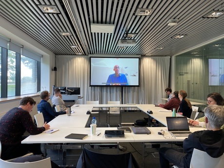 Picture of the workshop room with attendees around a boardroom style table watching Prof Zeray Yihdego presenting online at the 'Death and Law' Workshop