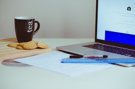 Image of open laptop with tea cup and biscuits on the side.