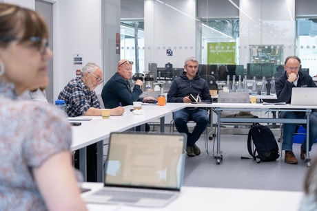 A group of people sitting round an U-shaped arrangement of desks talking and listening