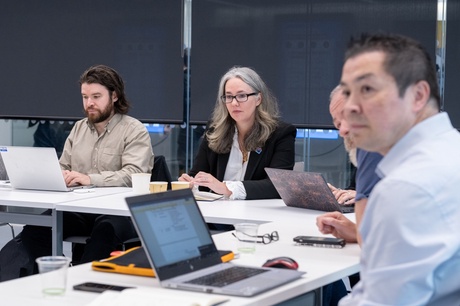 A group of people sitting round an U-shaped arrangement of desks talking and listening