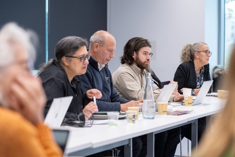 A group of people sitting round an U-shaped arrangement of desks talking and listening