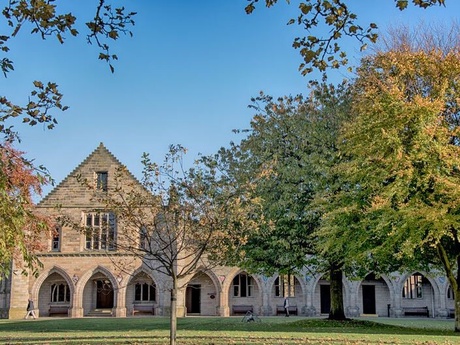 Elphinstone Hall and the cloisters seen from aross the lawn, with autumnal trees and a blue sky