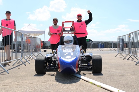 Two team members and the car with the driver in the seat