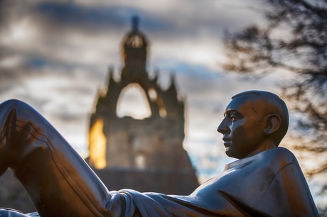 A statue of a youth reclining holding a split apple in front of King's College chapel at the University of Aberdeen