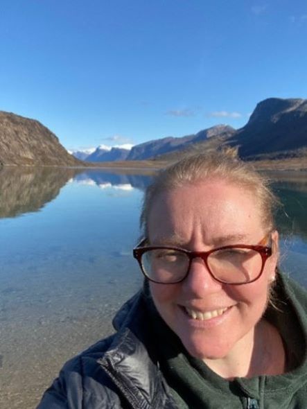 Dr Caughey in front of clear water, hills and blue sky
