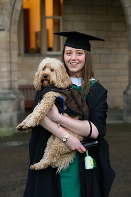 A woman in cap and gown holding her dog