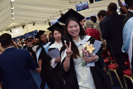 Graduates leaving the graduating marquee with the woman at the front of the queue giving a peace sign