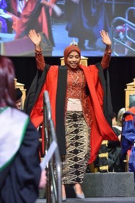 A woman walking off the graduation stage with her hands in the air