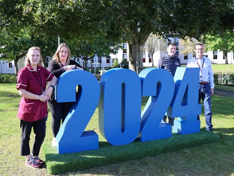 Four people standing beside large 2024 numbers