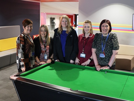 Five people standing beside a pool table