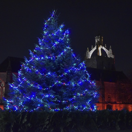 A photograph of a lit up Christmas tree at night with the King's College Crown in the background