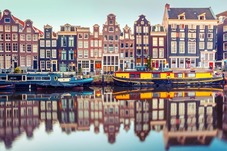 a canal with canal boats and traditional amsterdam row houses, the houses are reflected in the canal.