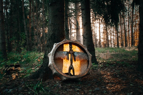 A shamanic drum, decorated with feathers and wooden decorations. It is leaning against a tree in a foerest..