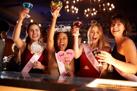 A group of four women in a bar raising their cocktail glasses in a 'Cheers' motion.