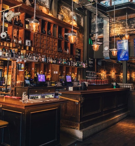 Image of traditonal bar with bar stools in front and various drinks and bottles on display behind.