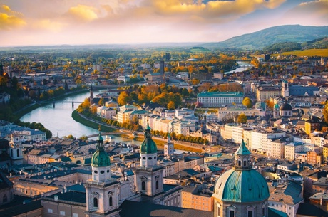 Picture of a city with mountains in the background, a river winding through a mixture of old and new buildings and multiple domed towers.