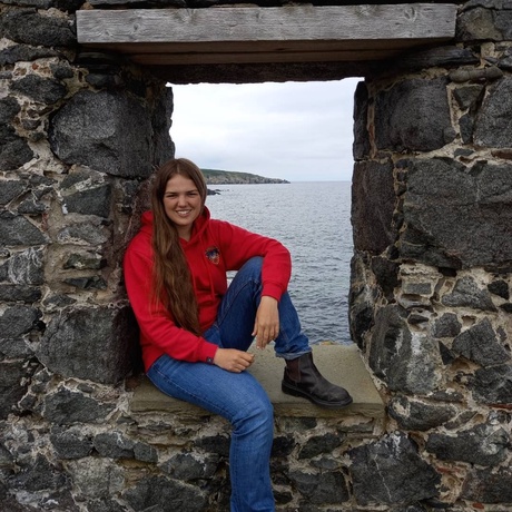 A young woman sitting in the window of a ruined granite building, with the North Sea in the background