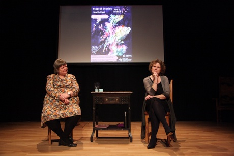 Two storytellers seated in front of a film projection