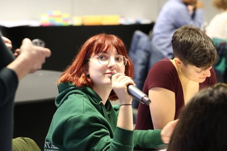 woman with microphone among other people in a conference room