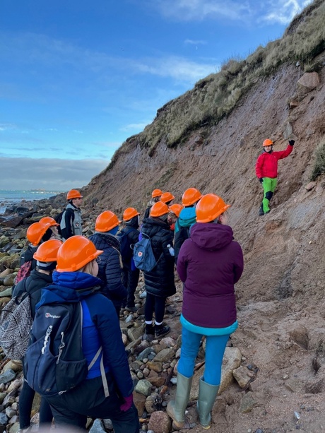 Students in the field wearing helmets looking at soil exposed on a hill