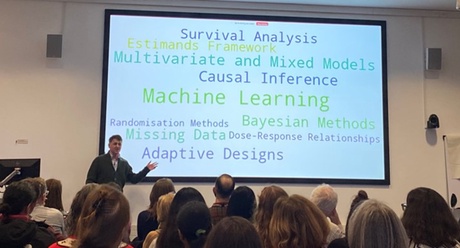 Graeme MacLennan presenting to an audience in front of a slide listing the names of statistical analyses,