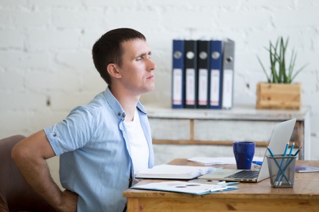 Man at work at desk holding his lower back