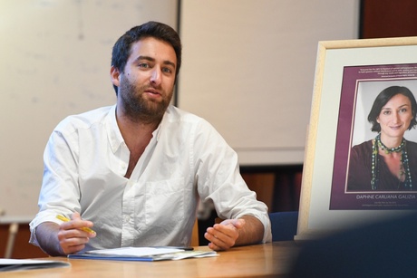 Matthew Caruana Galizia speaking next to a portrait of his mother at the University of Aberdeen'