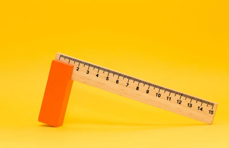 A ruler stands in the center, against a yellow background with an orange block