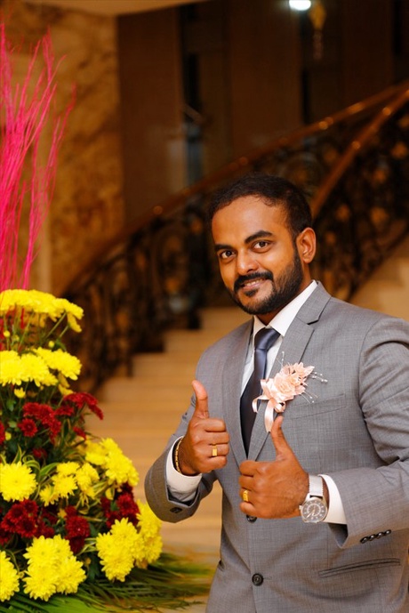 Camilo wearing a suit giving a thumbs up in front of a large bouquet of flowers