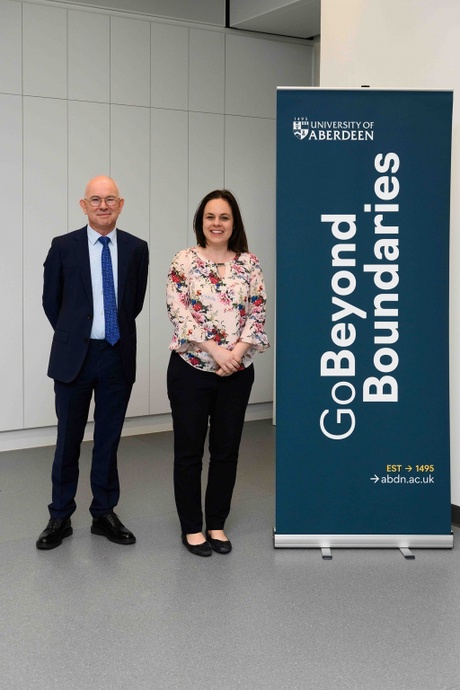 Two people standing and smiling beside a University of Aberdeen sign