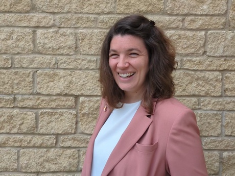 A smiling Dr Medaney in a pink jacket in front of a stone wall