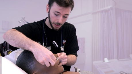 A medical student fixes a breathing aid to a training dummy in a hospital bed