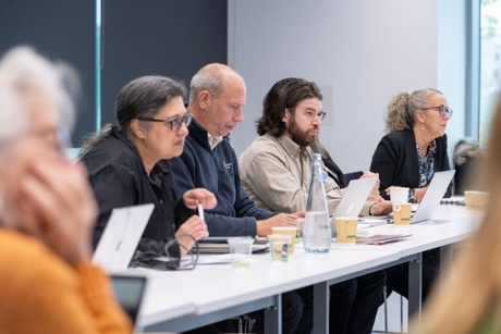 A group of people sitting round an U-shaped arrangement of desks talking and listening