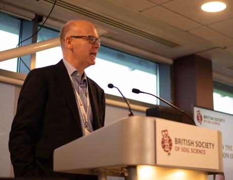 Professor Paul Hallet delivering a speech at a podium with the British Society of Soil logo