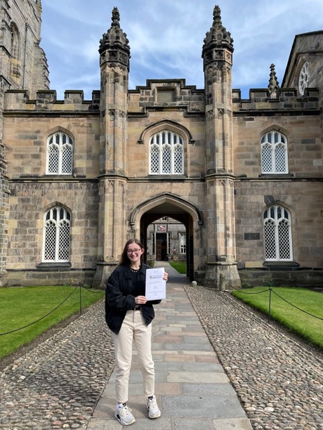 Rebecca stands in front of King's College holding her dissertation