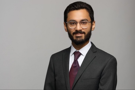 Syed in a suit standing in front of a grey background