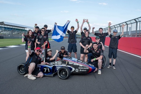 The TAU team with their car holding a Scottish flag with their arms in the air