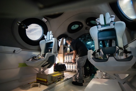 Inside the space craft - two seats for passengers and a man completing checks.