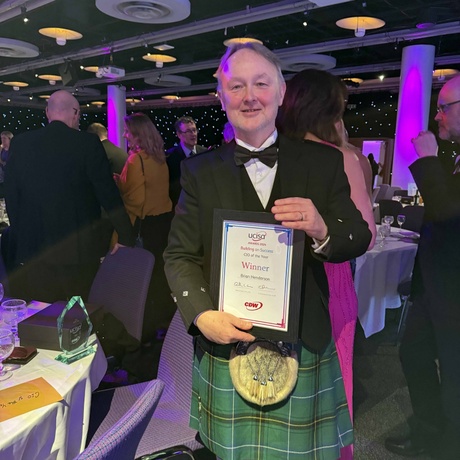 Gentleman in traditional Scottish outfit holding award