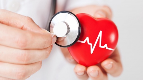 A doctor examining a model cartoon-style heart with a stethoscope