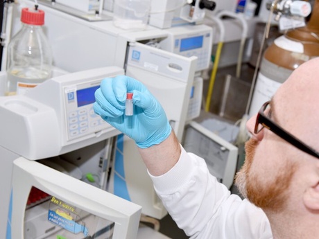 A lab assistant in a white coat and blue gloves holding up sample