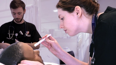 Medical student looks into a practice dummy's eyes with a a torch