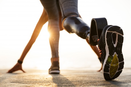 Back view of disabled athlete woman with prosthetic leg getting ready to run to run outdoor at the beach