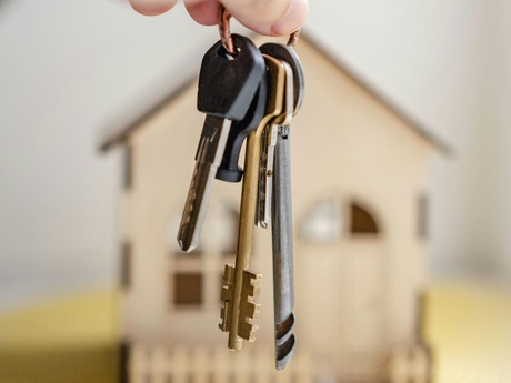 A hand dangling a bunch of keys in front of a blurred model of a house