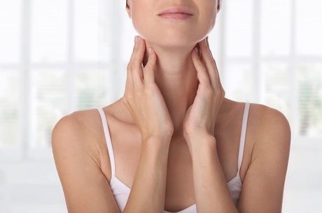 A woman in a white vest touching her neck and thyroid gland area